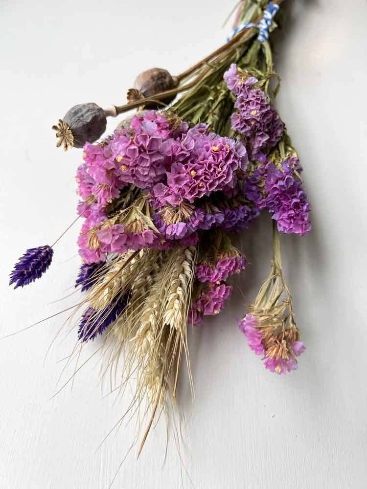 bunch of dried flowers containing lilac statice, poppy heads, wheat grass and purple phalaris.